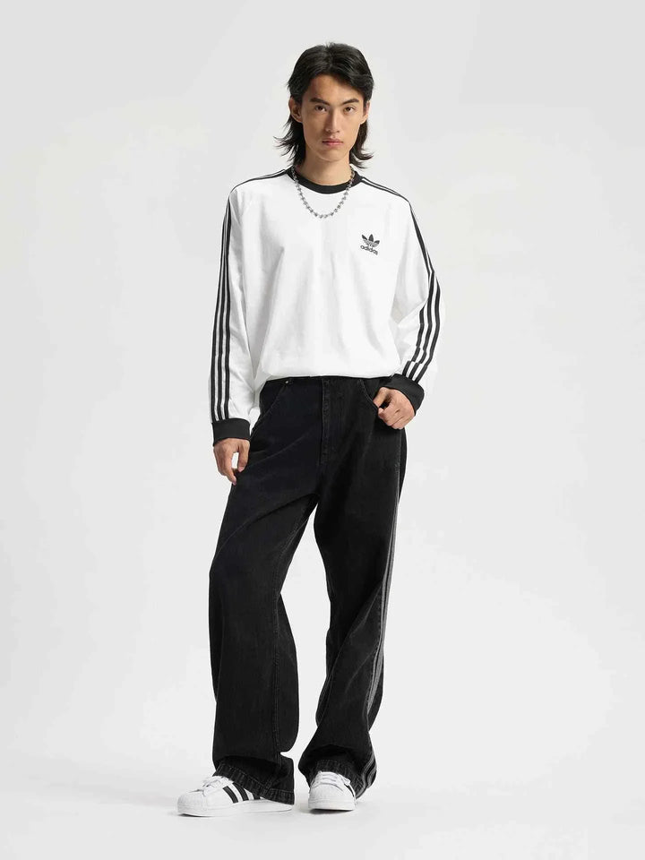 رجل يرتدي adidas تيشيرت قطني كلاسيكي بأكمام طويلة أبيض مع خطوط سوداء وشعار Trefoil على الصدر