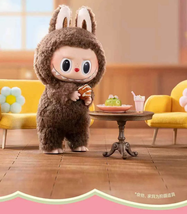 Labubu الأرنب الفخم من Pop Mart بإصدار Heart Macaron بجانب طاولة مع حلوى ومشروبات.