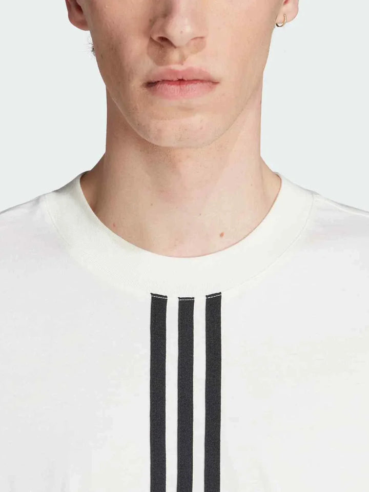 Close-up of a person wearing a white Adidas تيشيرت أديداس كلاسيك with three black stripes on the front, showcasing a soft cotton fabric and classic design.