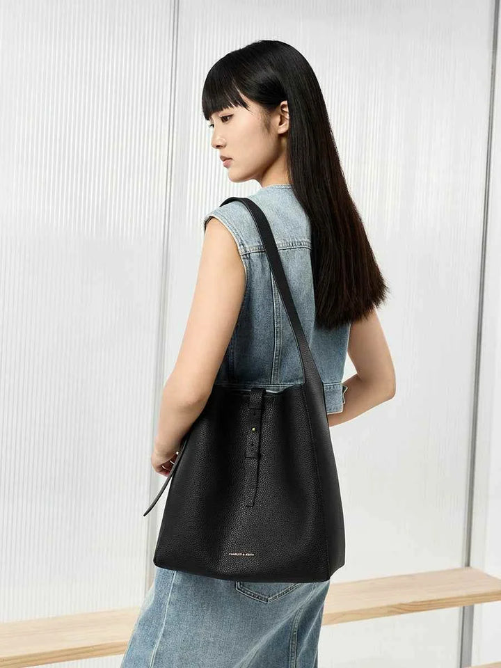 CHARLES KEITH black shoulder bag with adjustable strap and inner pouch, worn by woman in casual denim vest and skirt