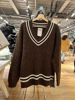Classic cable-knit winter sweater with striped edges in brown and white hanging on a wooden hanger in a store.