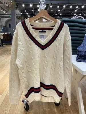 Classic cable knit winter sweater with striped edges in off-white displayed on hanger in store