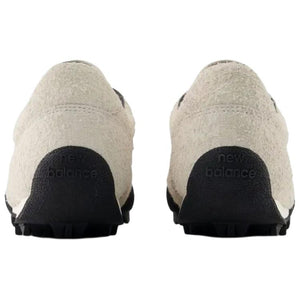 Rear heel view of a pair of Donald Glover x New Balance RC30 "Sea Salt" shoes, featuring textured hairy beige suede heels, dark collar linings, and an extended black rubber outsole wrap stamped with "new balance" text branding.