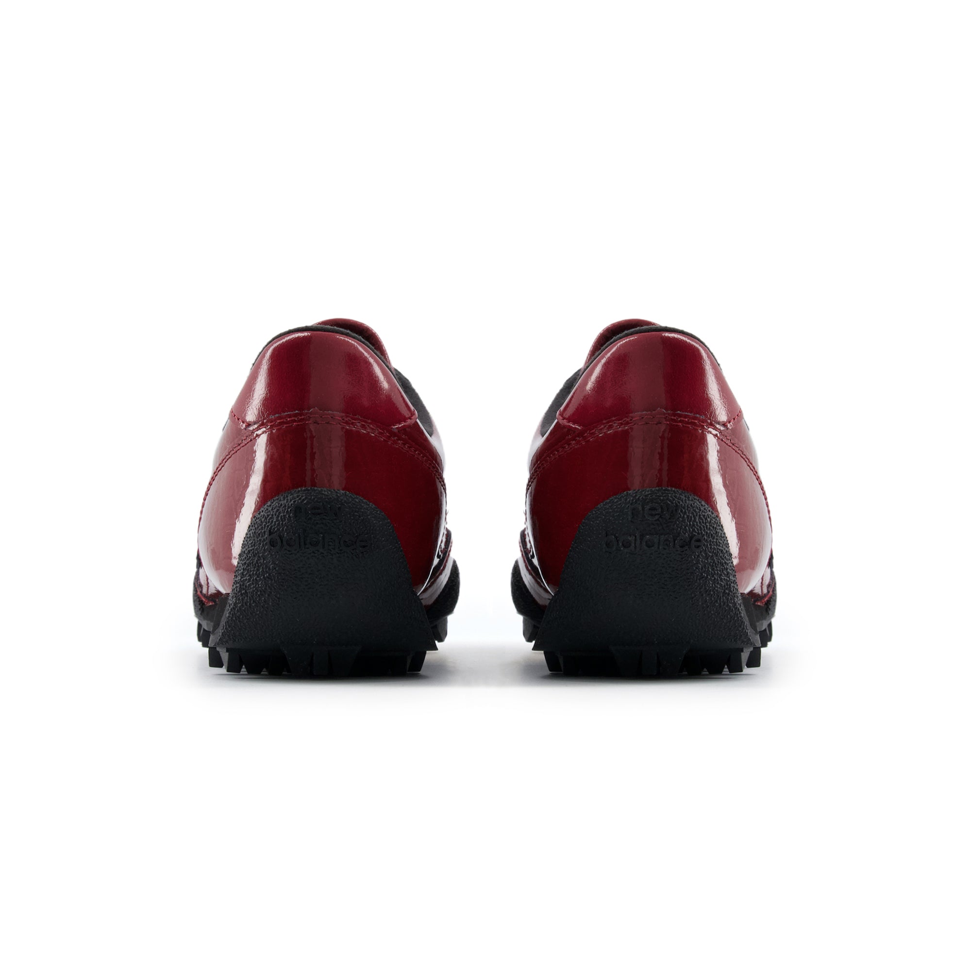 Rear heel view of a pair of burgundy patent leather New Balance RC30 shoes, featuring glossy burgundy heels, black interior linings, and an extended black rubber outsole wrap stamped with "new balance" text branding.