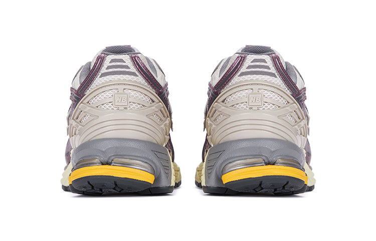 Rear heel view of a pair of grey and purple New Balance shoes 1906R model, featuring light beige molded TPU support cages with square NB branding, metallic mauve trim accents, off-white mesh collars, grey padded lining, and cream N-ergy cushioned midsoles with vibrant orange heel pods.