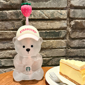 Front view of the clear Starbucks strawberry bear cup next to a slice of cheesecake, highlighting the details of كوب ستاربكس الدبدوب الوردي 2026 آخر اصدار.