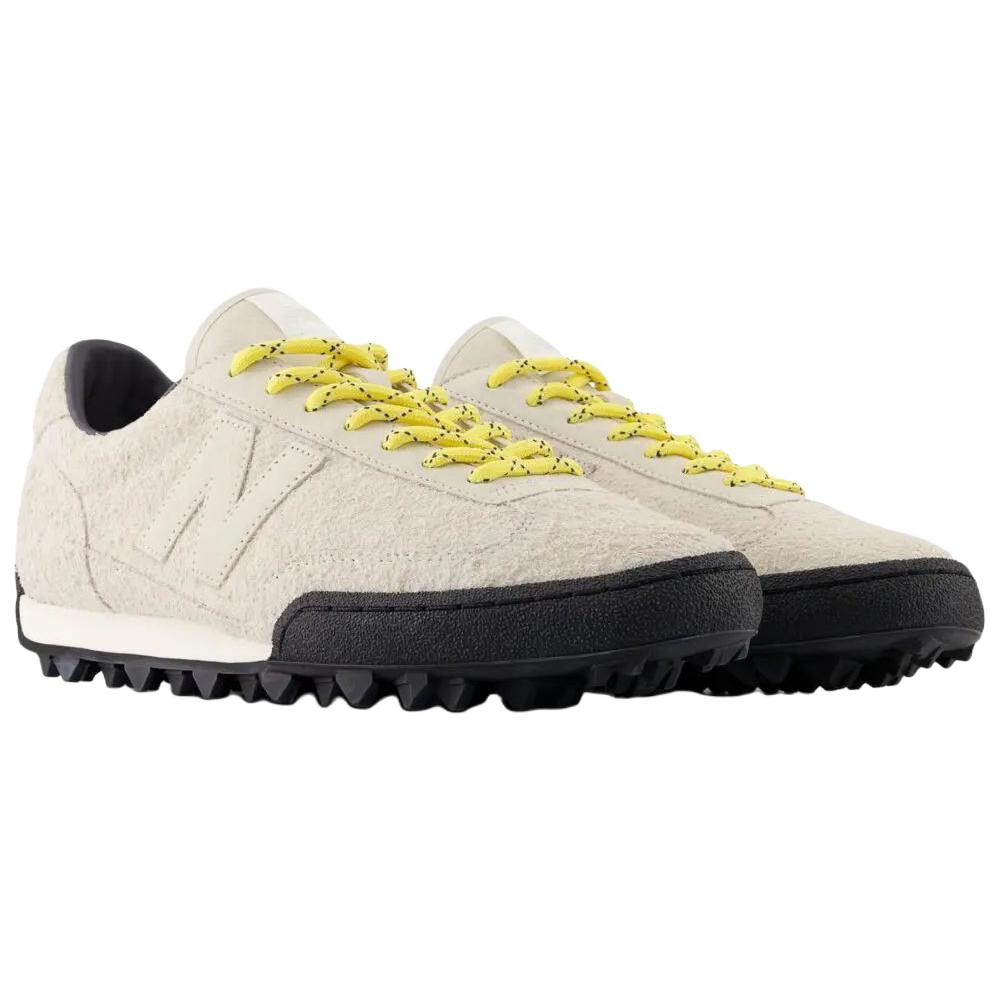 Three-quarter profile shot of a pair of Donald Glover x New Balance RC30 "Sea Salt" shoes, featuring textured hairy beige suede uppers, light beige suede N logos, vibrant speckled yellow laces, dark interior linings, off-white midsoles, and black rippled studded rubber outsoles.