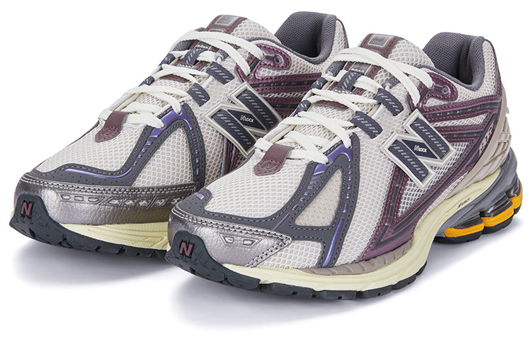 Three-quarter profile shot of a pair of grey and purple New Balance shoes 1906R model, featuring off-white mesh uppers, metallic mauve and slate grey overlays, cream laces, dark grey collar lining, and cream N-ergy cushioned midsoles with orange heel pods.