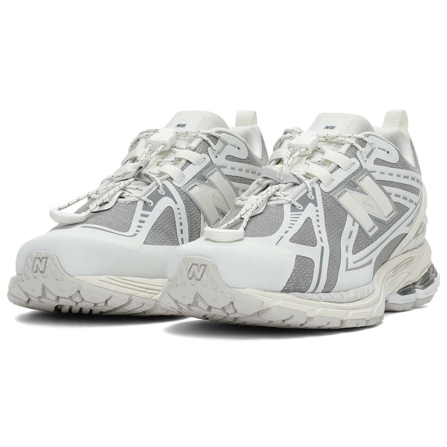 Three-quarter profile shot of a pair of grey and white New Balance shoes 1906R model, featuring grey textured mesh uppers, white and silver overlays, white toggle speed lacing system, heel pull tabs, and white N-ergy cushioned midsoles with silver heel pods.