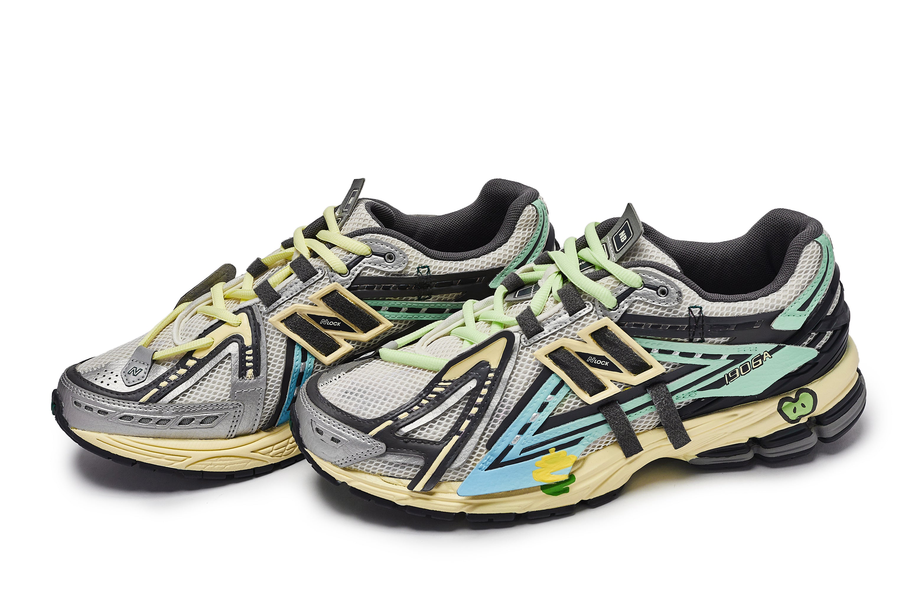 Three-quarter profile shot of a pair of grey, green, and blue New Balance shoes 1906A model, featuring light grey mesh uppers, deconstructed multi-colored synthetic overlays, mint green laces, light blue panels, dark grey collar lining, and aged yellow N-ergy cushioned midsoles with graphic details.