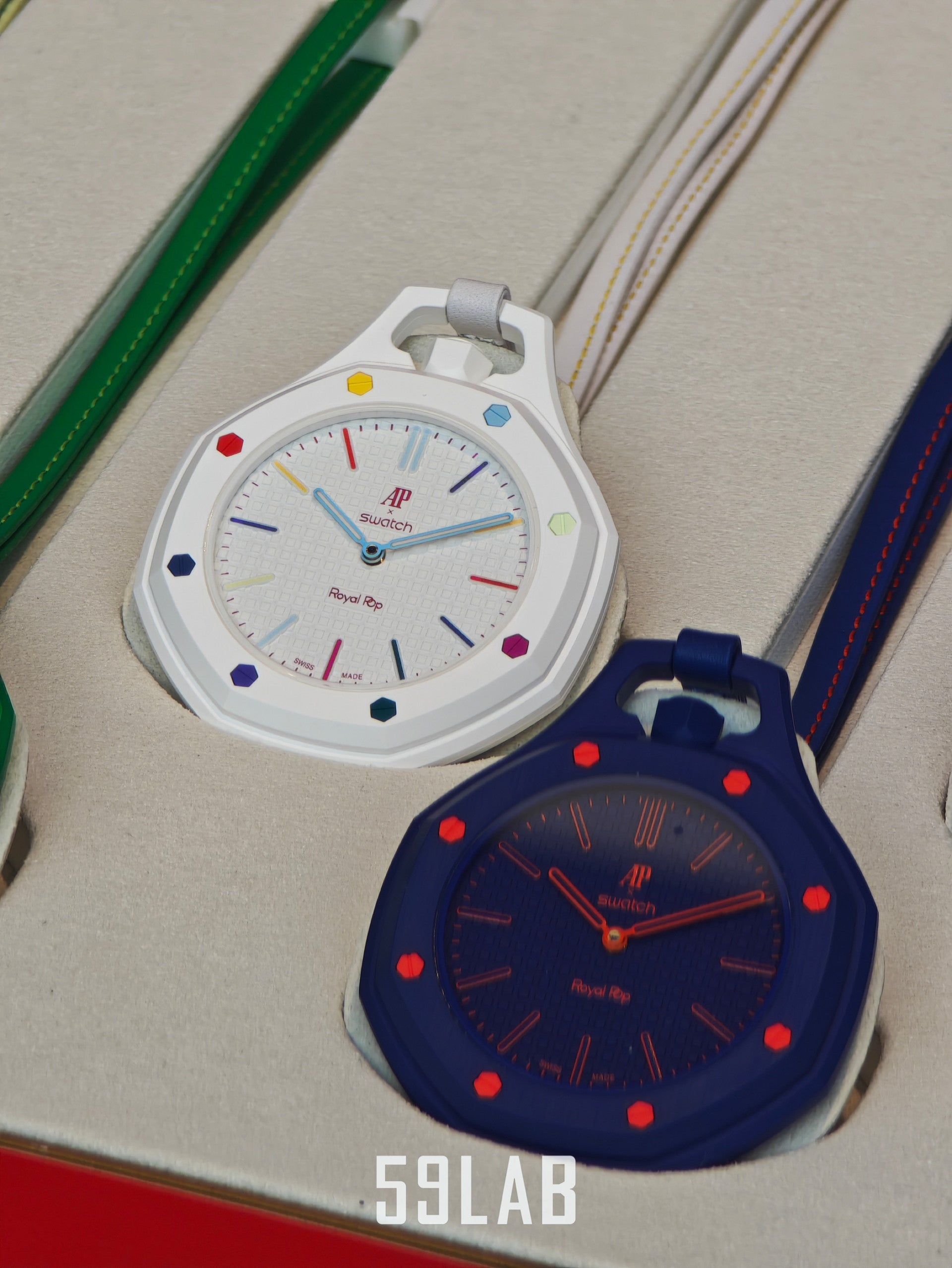 Two Audemars Piguet x Swatch Royal Pop bioceramic pocket watches in matte white and dark navy blue resting on their retail box.