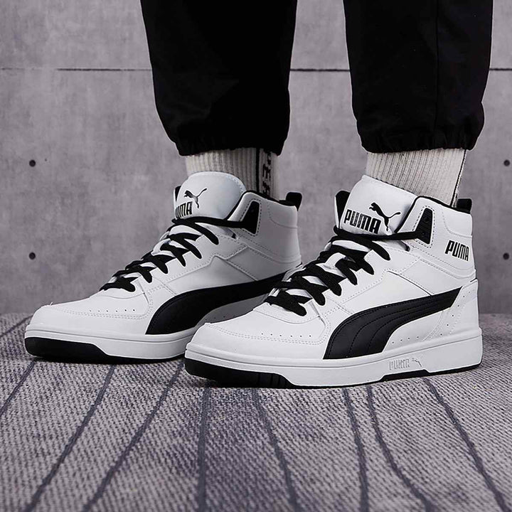 Puma high top sneakers in white and black on a textured floor, offering ankle support and sporty style.