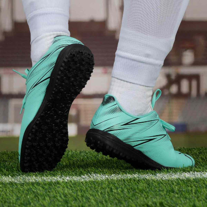 Puma turquoise and black football shoes on artificial grass surface.
