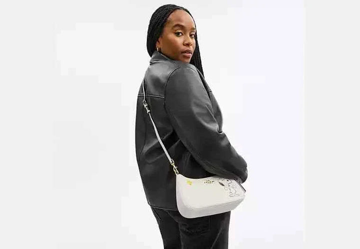 Terry shoulder bag by Coach X Peanuts featuring Snoopy design, worn by a person.