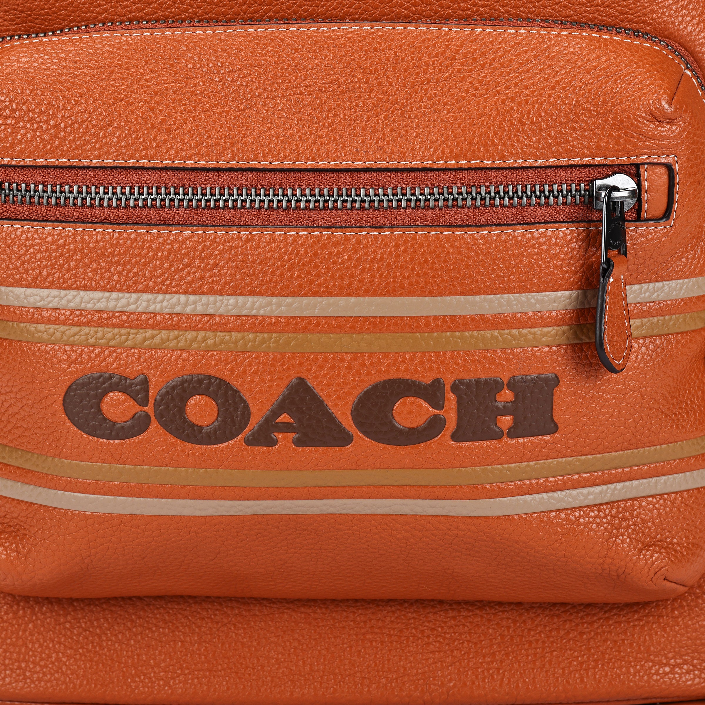 Detailed close-up of the printed Coach logo and metallic zipper on the front pocket of a brown genuine leather backpack.

لقطة قريبة مكبرة لشعار Coach المطبوع والسحاب المعدني على الجيب الأمامي لحقيبة ظهر من الجلد الطبيعي بني.