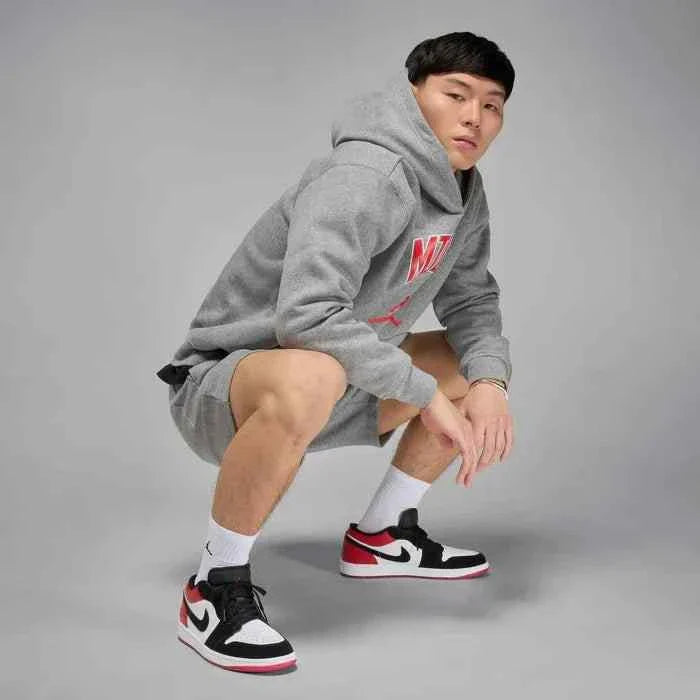 Air Jordan 1 Low sneakers in white, varsity red, and black worn by a person in a grey outfit.