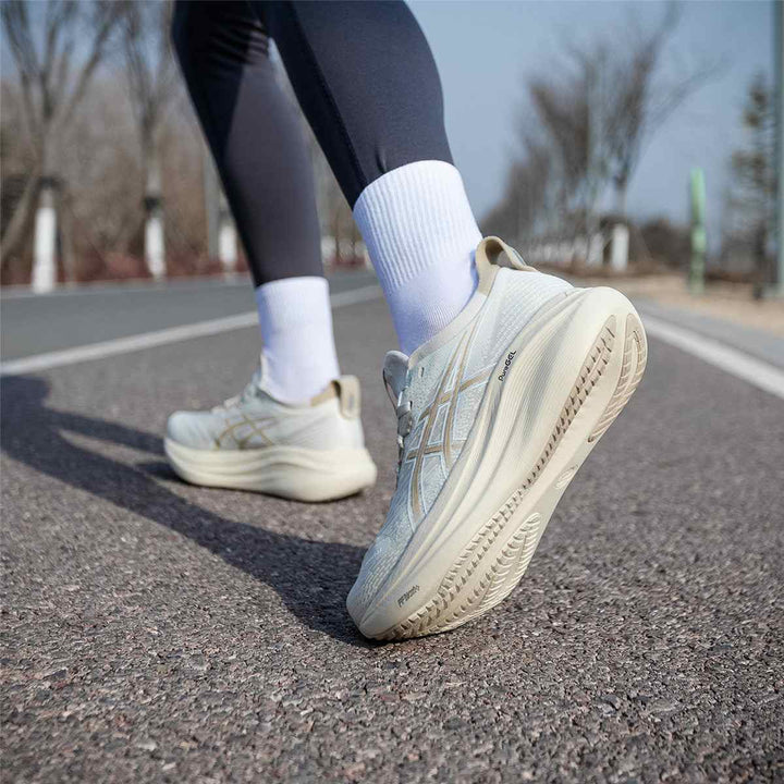 ASICS Gel-Nimbus 27 beige running shoes on asphalt road.