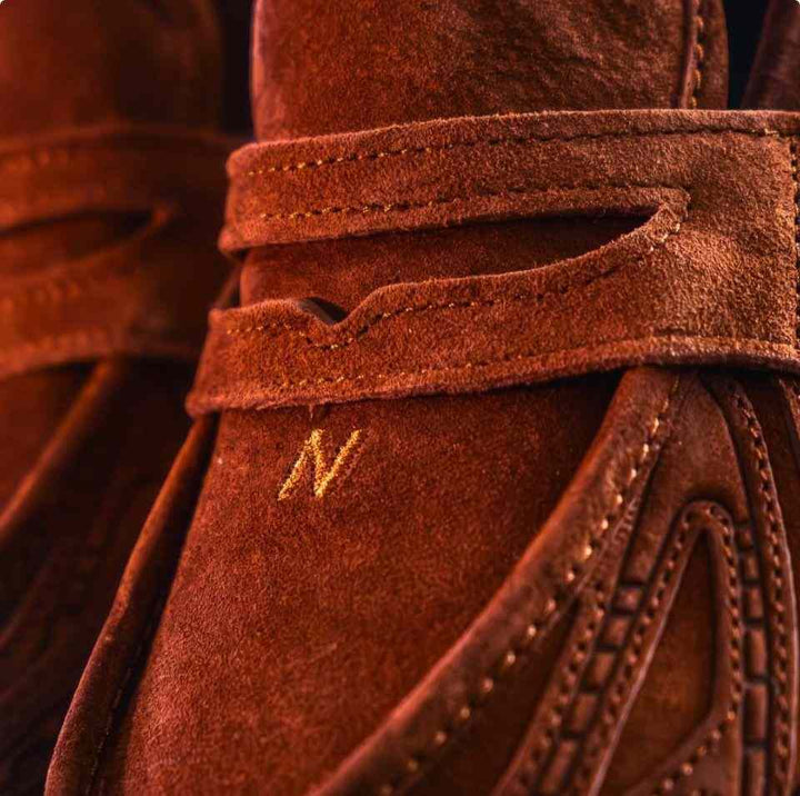 Close-up of brown New Balance 1906 suede sneaker with stitched "N" logo and textured strap detail