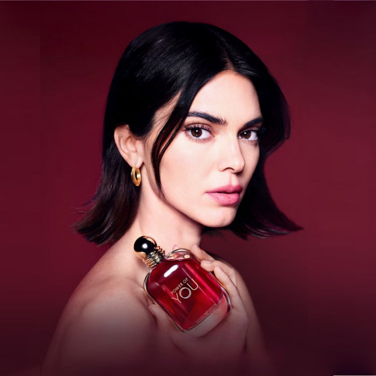 A sophisticated woman holding the power of you armani original perfume bottle close to her shoulder during an elegant beauty campaign photoshoot.