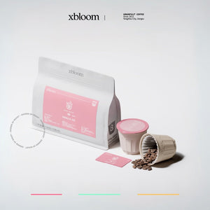 A clean studio shot of xBloom xpods showing the specialty coffee packaging, a single capsule, and roasted coffee beans flowing out of a pod, perfect for showcasing كبسولات إكسبلوم on a light grey background.