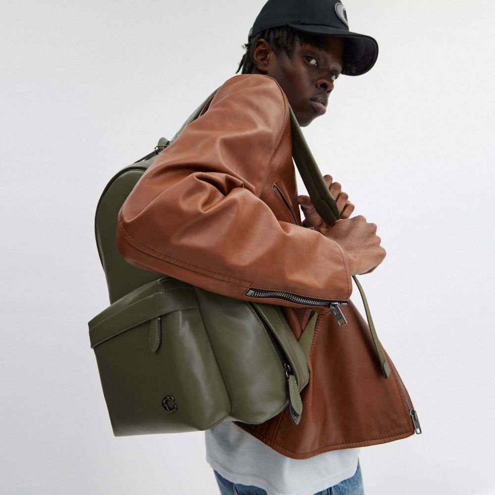 Side view of a man wearing an authentic Coach Westway 32 olive green leather backpack, perfect for back-to-school and casual styling.

عرض جانبي لرجل يرتدي حقيبة ظهر كوتش ويست واي 32 أصلية جلد باللون الزيتي، مناسبة للعودة للمدرسة والإطلالات العصرية.