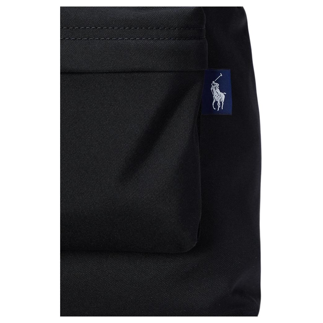 Detailed close-up of the woven navy blue pony logo tag on the side pocket of an authentic black Polo Ralph Lauren backpack.

لقطة قريبة مكبرة لعلامة شعار المهر المنسوجة باللون الكحلي على الجيب الجانبي لحقيبة ظهر Polo Ralph Lauren أصلية باللون الأسود.