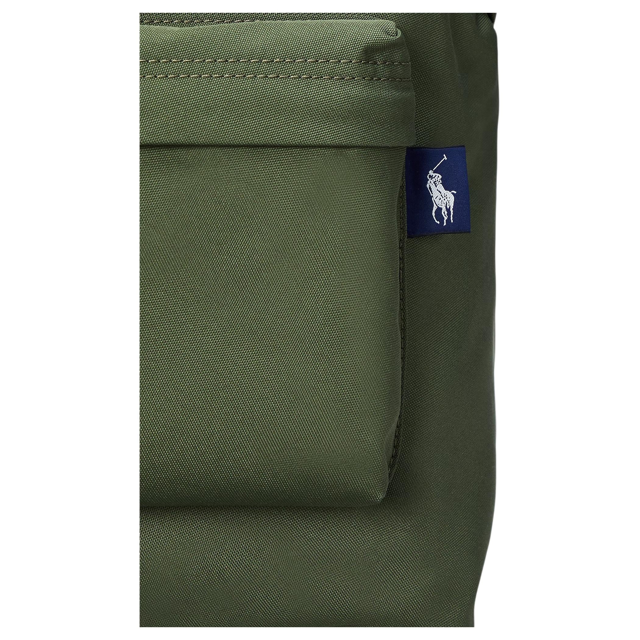 Detailed close-up of the woven navy blue pony logo tag on the side pocket of an authentic olive green Polo Ralph Lauren backpack.

لقطة قريبة مكبرة لعلامة شعار المهر المنسوجة باللون الكحلي على الجيب الجانبي لحقيبة ظهر Polo Ralph Lauren أصلية باللون الأخضر الزيتوني.