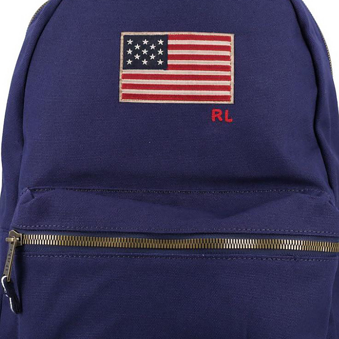 Close-up detail of the embroidered US flag patch, RL initials, and metallic brass zipper on an original Ralph Lauren navy blue backpack.

لقطة قريبة لمكعبات تطريز رقعة العلم الأمريكي وأحرف RL والسحاب النحاسي المعدني على حقيبة ظهر رالف لورين أصلية باللون الكحلي