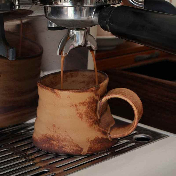 كوب فخار مائل بتصميم ريفي بني وعسلي على ماكينة قهوة.