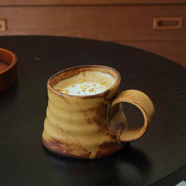 كوب فخار مائل بتصميم فني ولون دافئ من البني والعسلي.