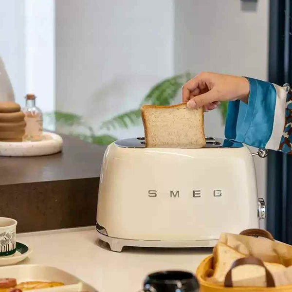 سميج Cream SMEG Italian toaster with a hand inserting bread slice on kitchen counter