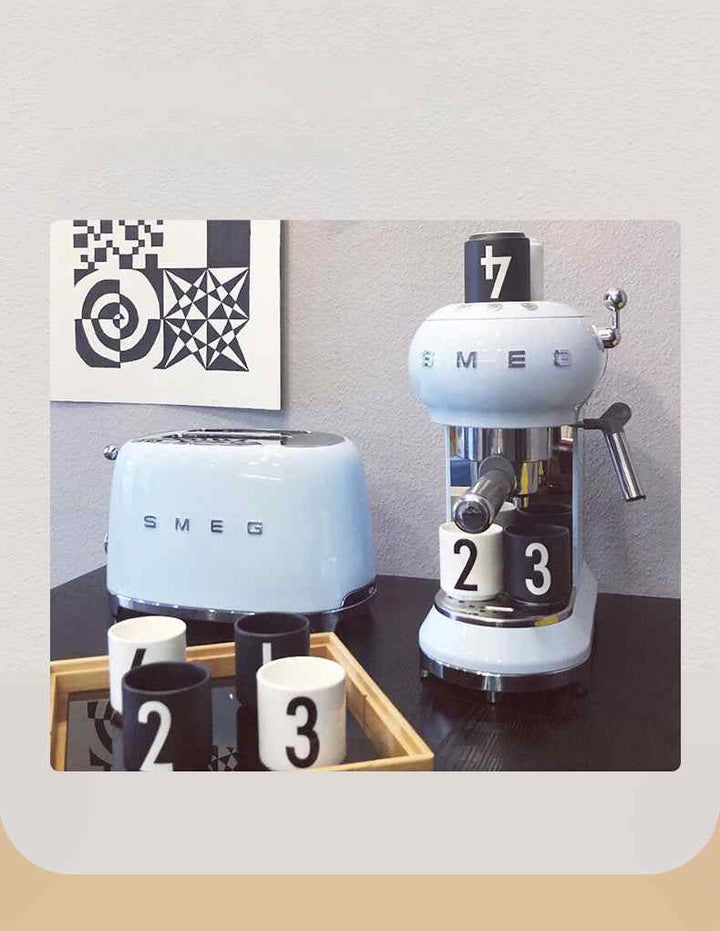 Light blue SMEG TSF02 toaster with retro design on kitchen counter next to matching coffee machine and numbered cups