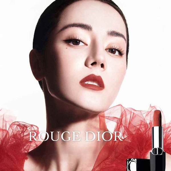 Woman wearing classic Rouge Dior lipstick with elegant red tulle background and Rouge Dior lipstick tube.