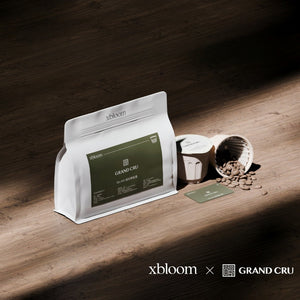 A white coffee bag and xBloom capsules of Ethiopia Elto Songo Project by Grand Cru, displayed on a wooden surface with scattered coffee beans.